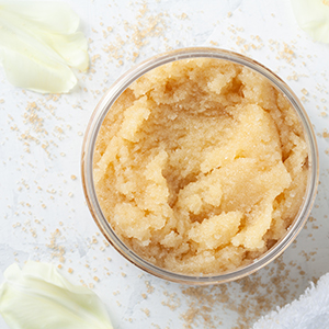 Closeup of a container with body scrub in it, and petals sitting on the table nearby.
