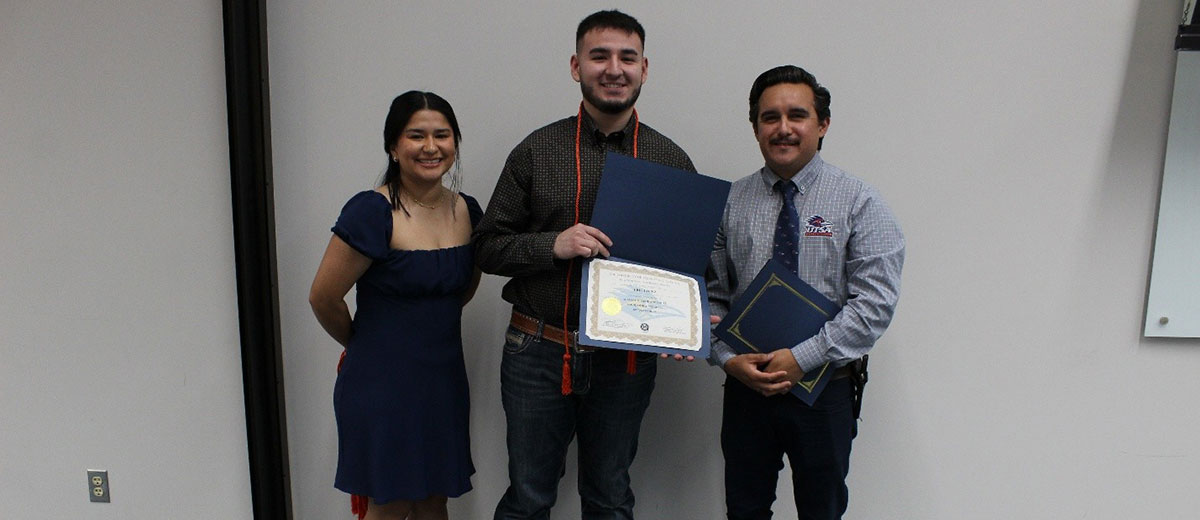 Three people with the one in the middle showing a certificate