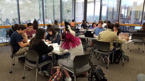 Several students gathered around tables in the Writing Center working on laptops during a workshop